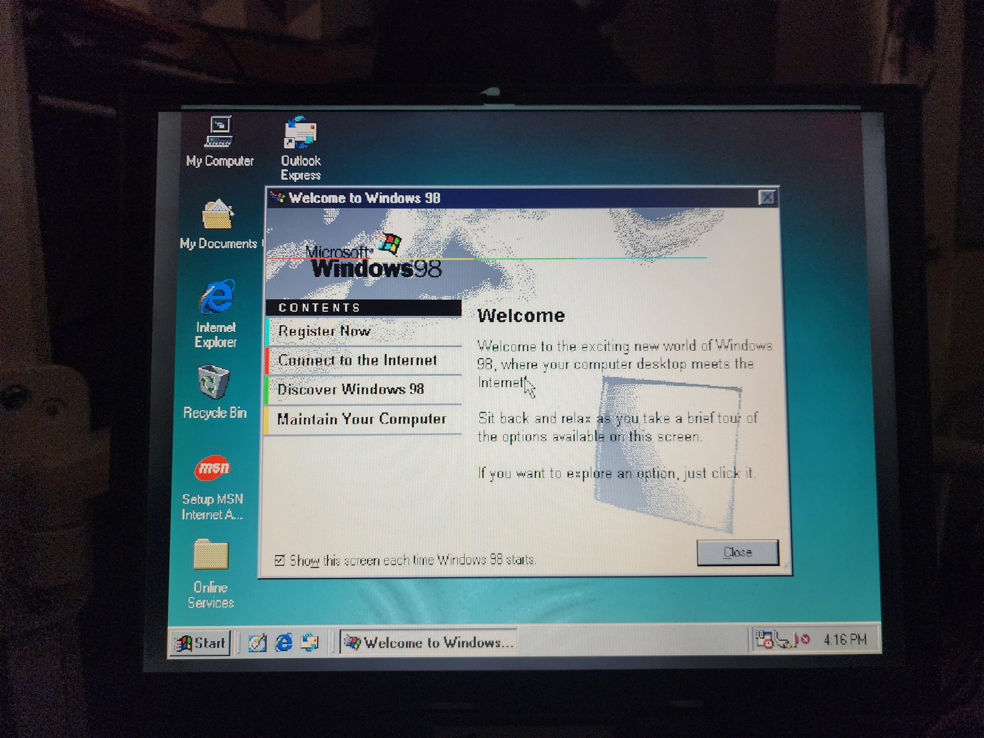 A laptop screen showing the Welcome to Windows 98 dialog on a Windows 98 desktop 