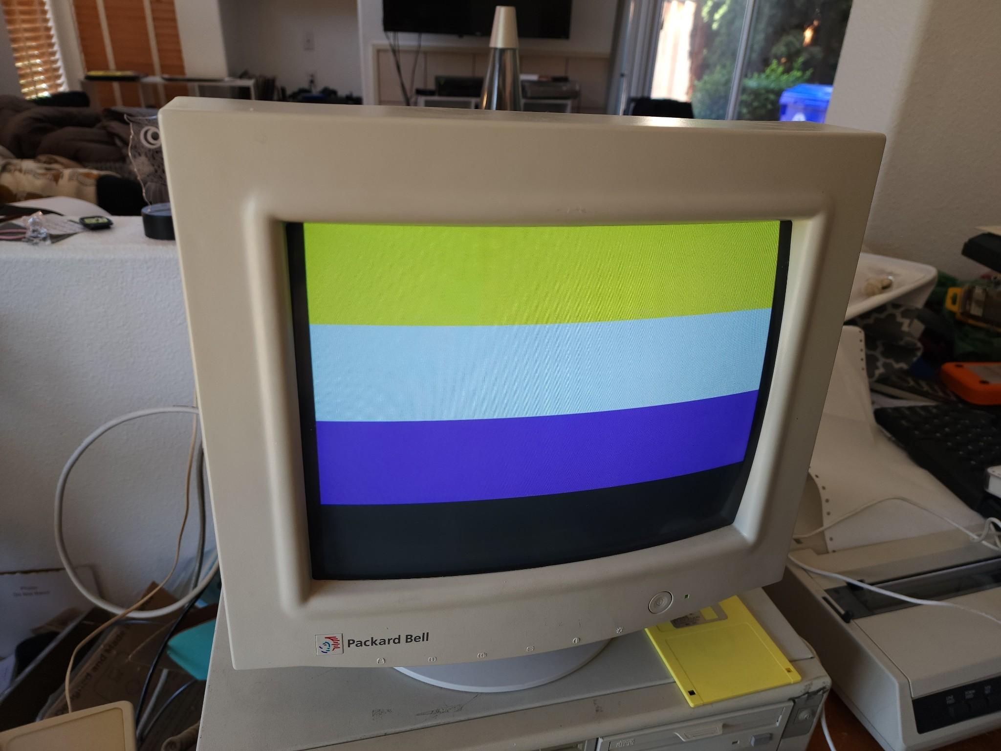 A beige 90s computer displaying the non-binary flag (four horizontal stripes, of yellow, white, purple, and black)